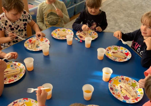 6 urodziny Zosi. Dzieci siedzą przy stole i jedzą widelczykami tort. Obok tależyków stoją kubeczki z sokiem.
